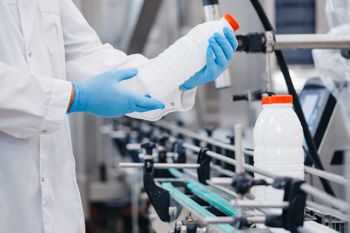 Person in clean white lab coat and blue latex gloves inspecting a bottle of liquid