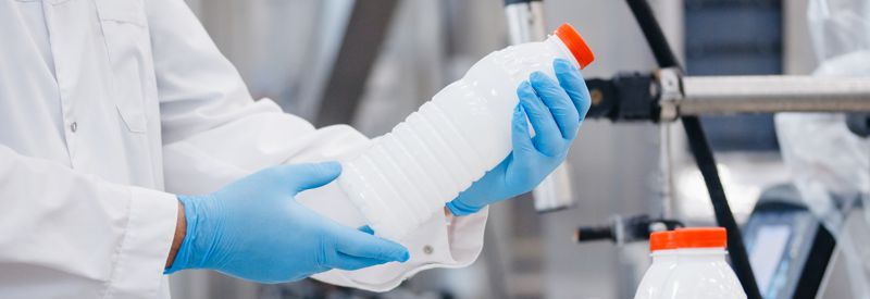 Person in clean white lab coat and blue latex gloves inspecting a bottle of liquid