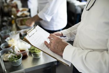 Person holding a clipboard and pen while evaluating food